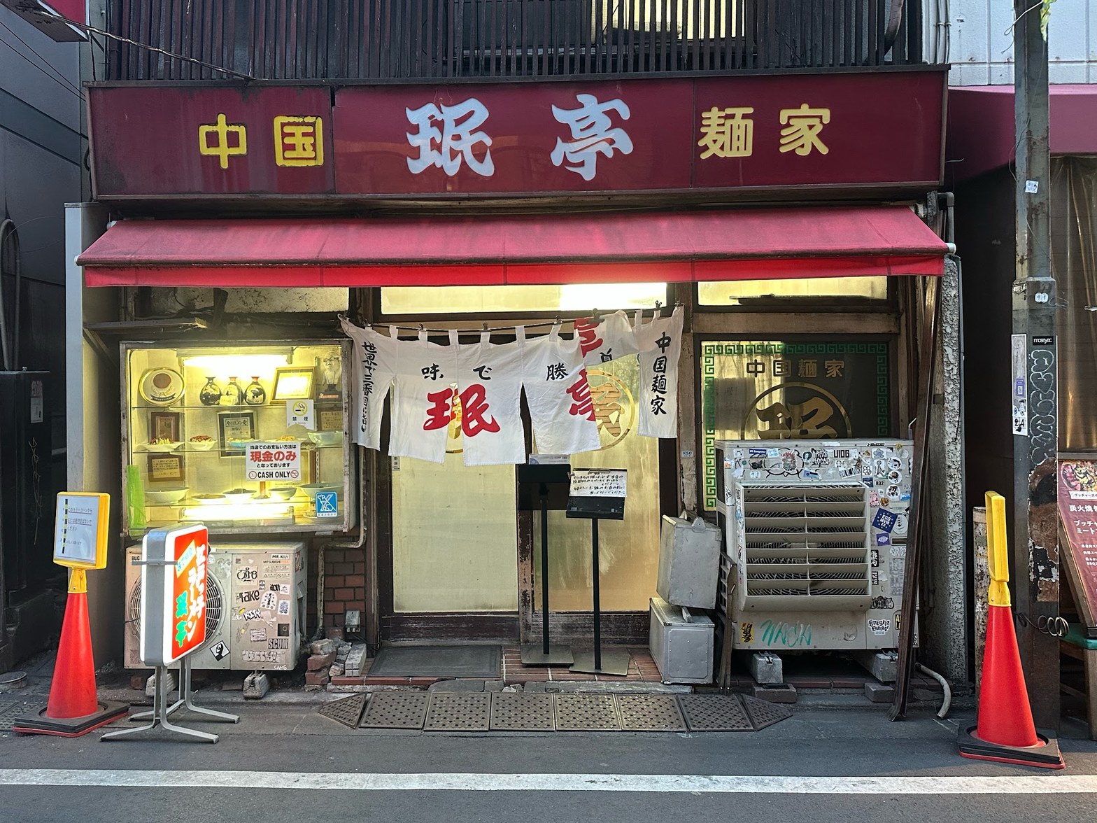 赤いひさしと金文字の「中国珉亭麺家」看板、白い暖簾が下がる路面店の正面外観