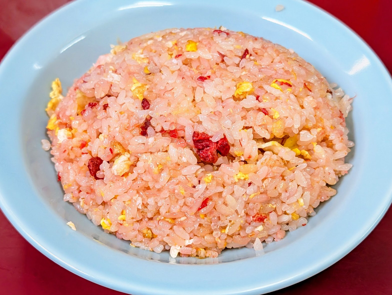 淡青色の皿に山盛りになったピンク色の炒飯。赤いチャーシューの粒が全体に散り、黄色い卵が混じる